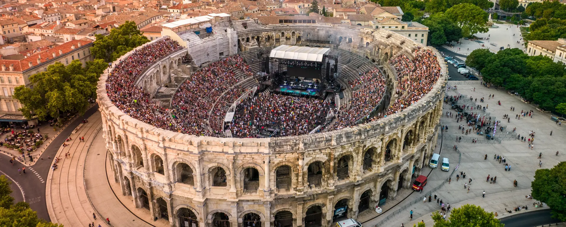 Vivre à Nîmes — vue aérienne des Arènes pleines pour un concert, au cœur de la ville