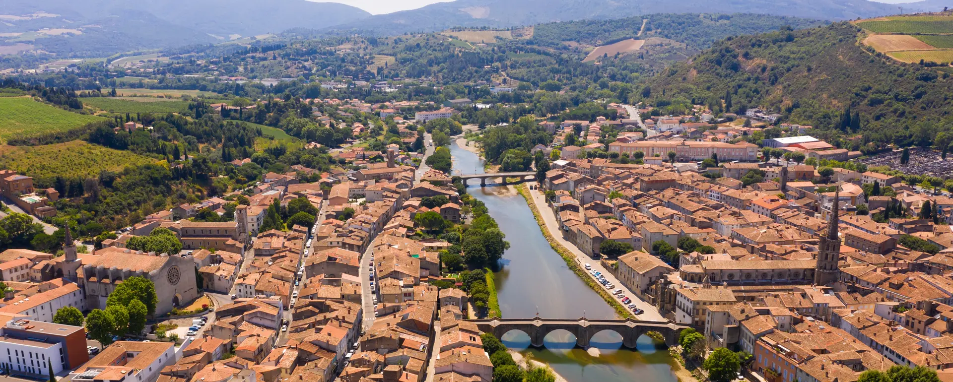 Vivre à Limoux — vue aérienne de la ville traversée par l'Aude, avec le Pont Neuf, l'église Saint-Martin et les coteaux viticoles