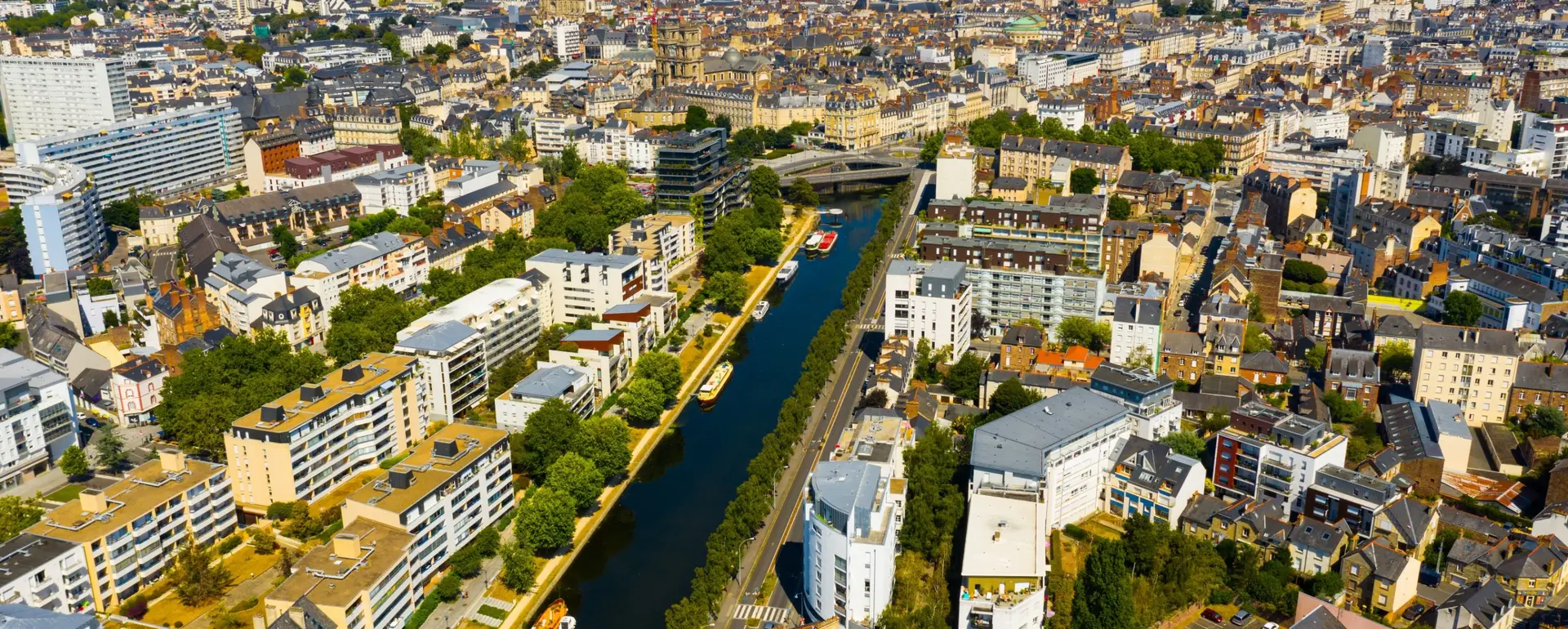 Vivre à Rennes — vue aérienne d'une voie d'eau bordée d'arbres, de péniches et d'immeubles, avec le centre ancien au loin